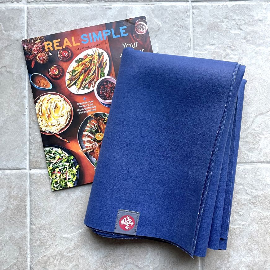 Folded navy yoga mat with a magazine for scale