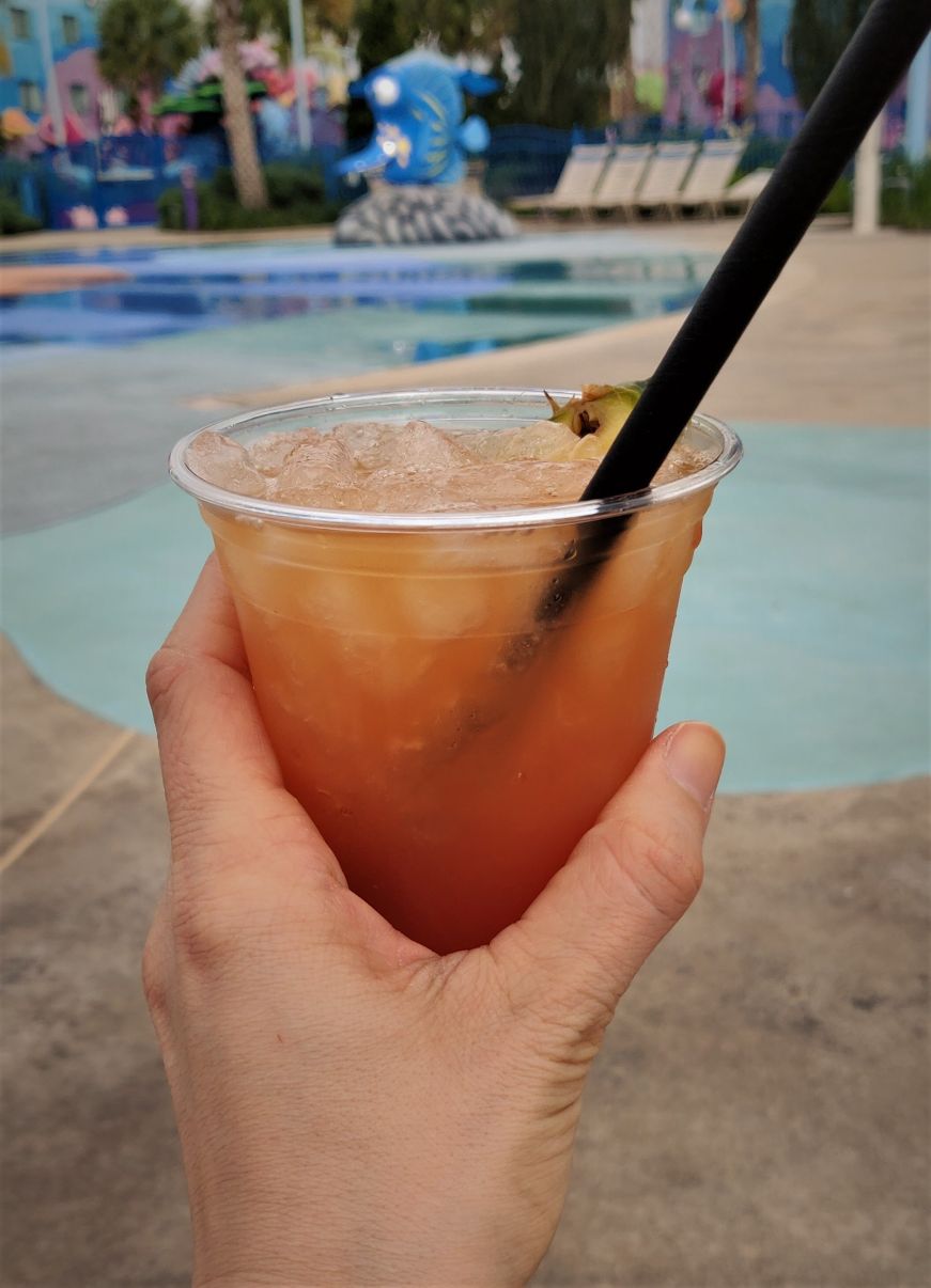 Hand holding mai tai with pool in the background, Art of Animation Resort