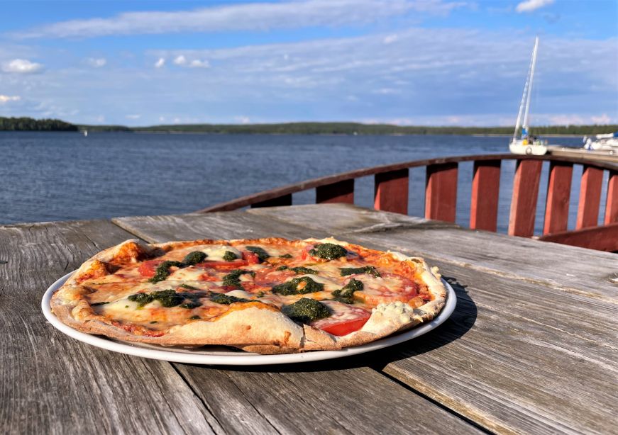 Margherita pizza sitting on a wooden table with a lake in the background
