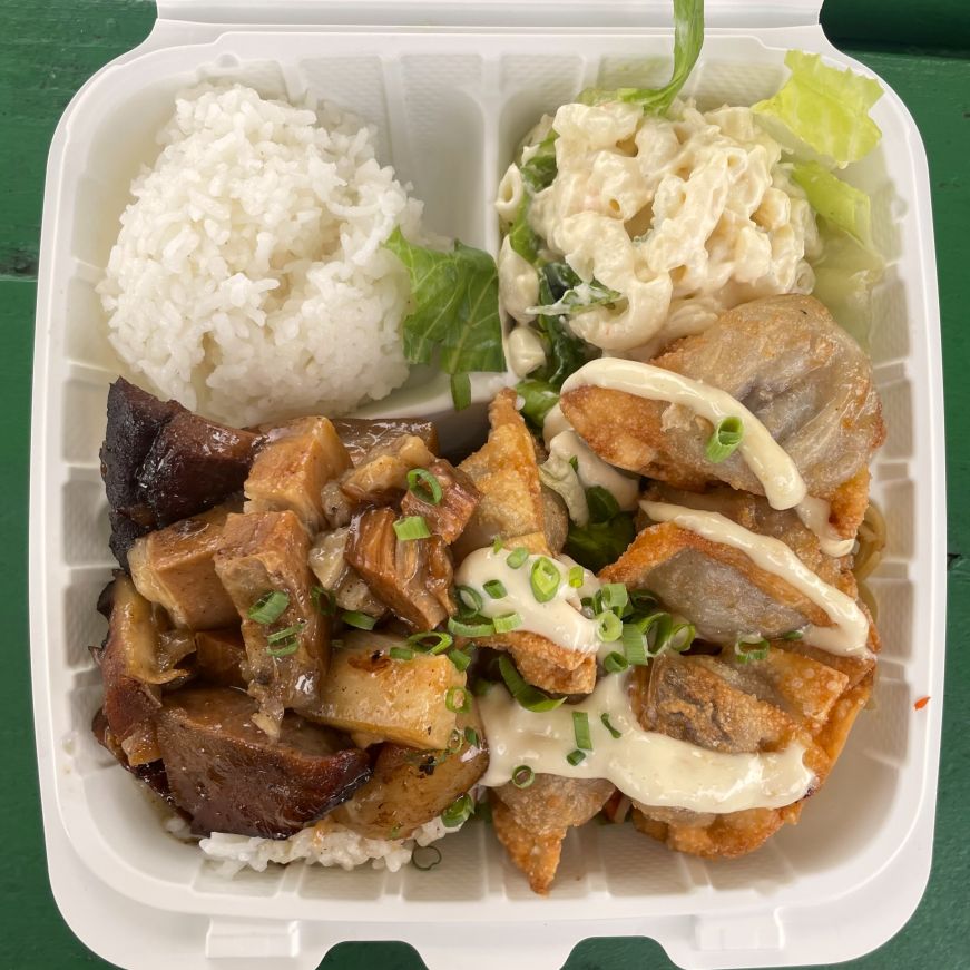 Top down view of a takeout container with rice, macaroni salad, dumplings, and pork belly