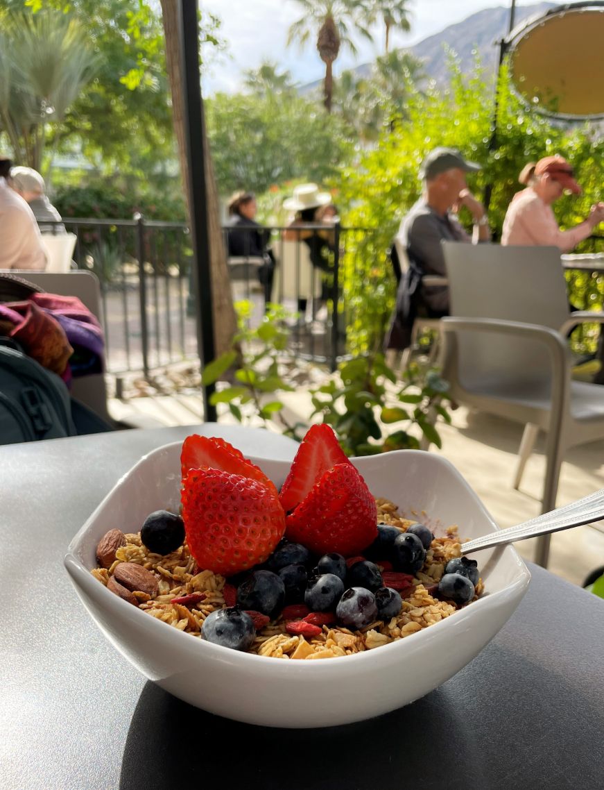 Acai bowl topped with granola and fresh fruit, sitting on a table in a courtyard with mountains in the background
