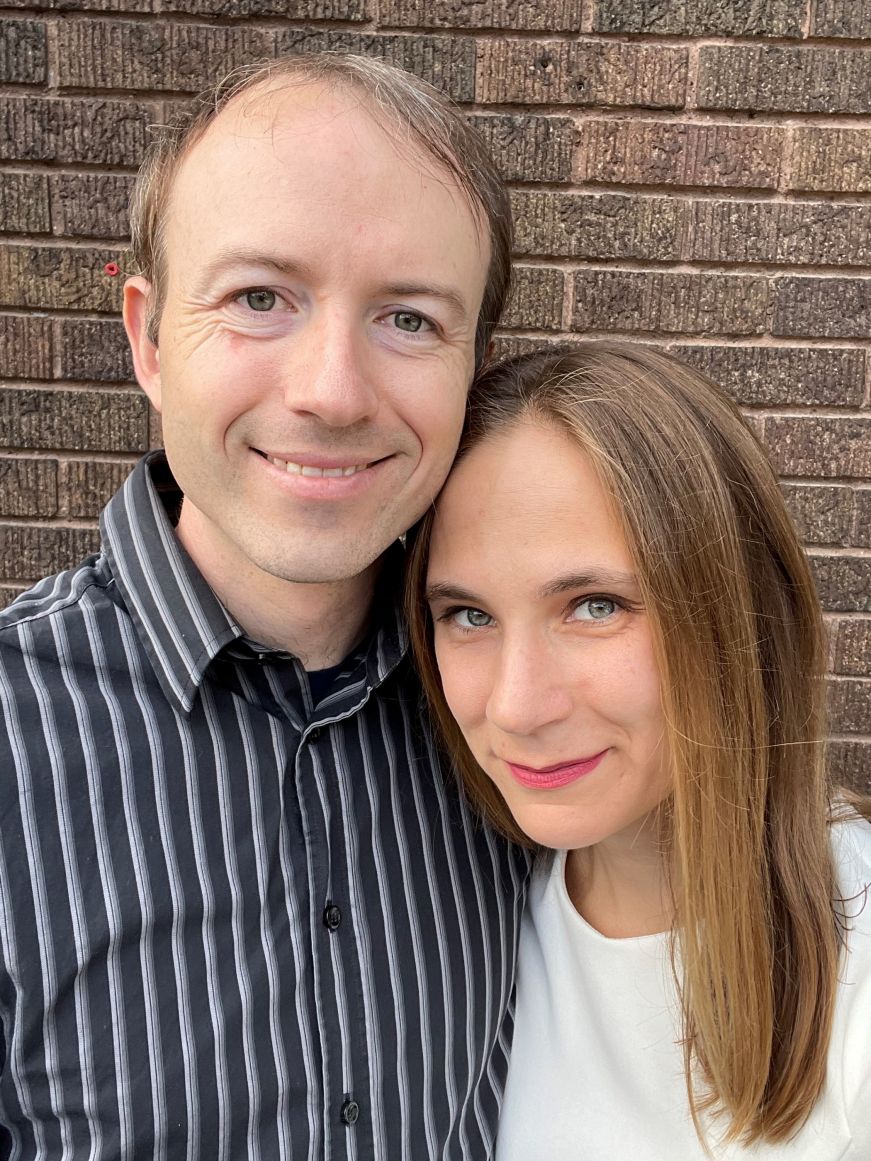 Mike and Stacy wearing dress clothes and standing in front of a brick wall