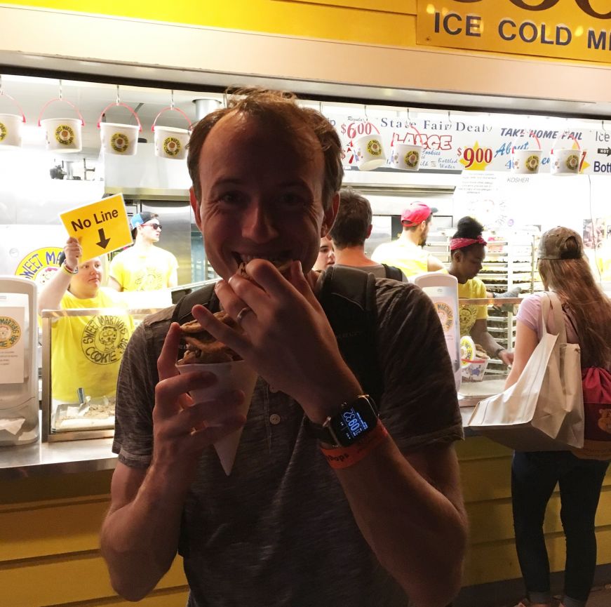 Mike eating a cone of chocolate chip cookies at night in front of the Sweet Martha's booth
