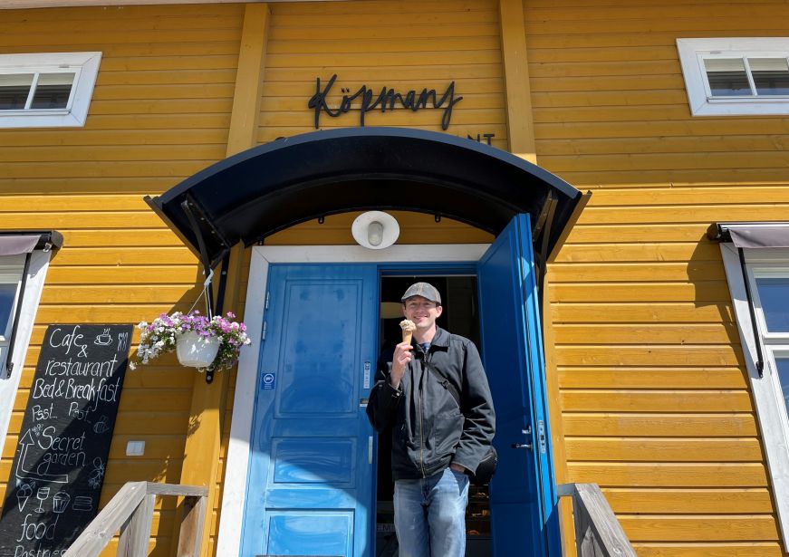 Mike eating gelato at Köpmans Cafe & Restaurant, Nagu Mike with an ice cream cone in front of a yellow building with a blue door