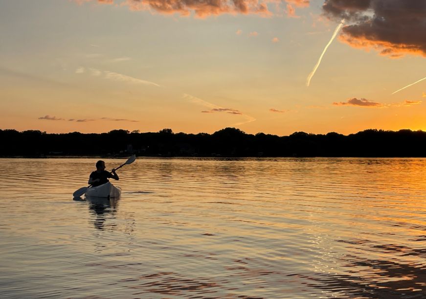 Mike paddling a kayak with a sunset in the background