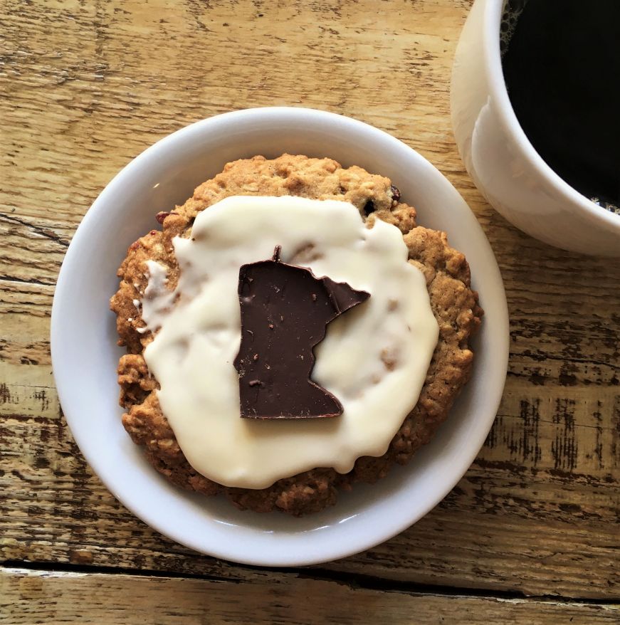Large oatmeal cookie topped with frosting and a Minnesota-shaped chocolate