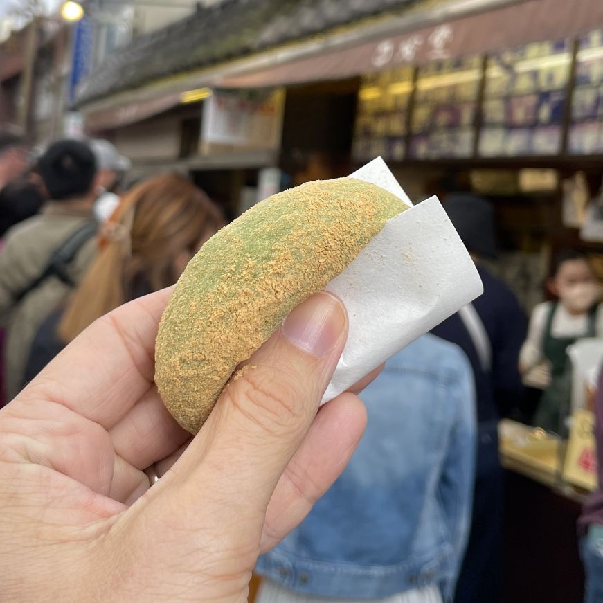 Hand holding a green mochi dusted with soy powder