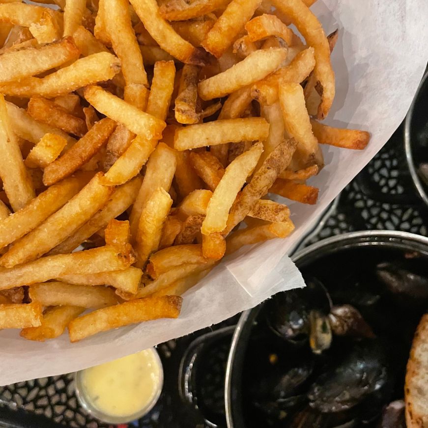 Top down view of a bowl of fries with a bowl of mussels in the background