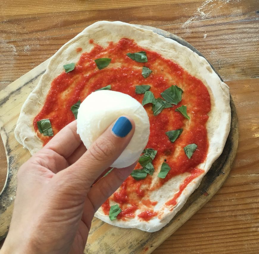 Hand holding a ball of mozzarella over a pizza topped with sauce and basil leaves, 1889 Pizza Napoletana, Kansas City, Kansas