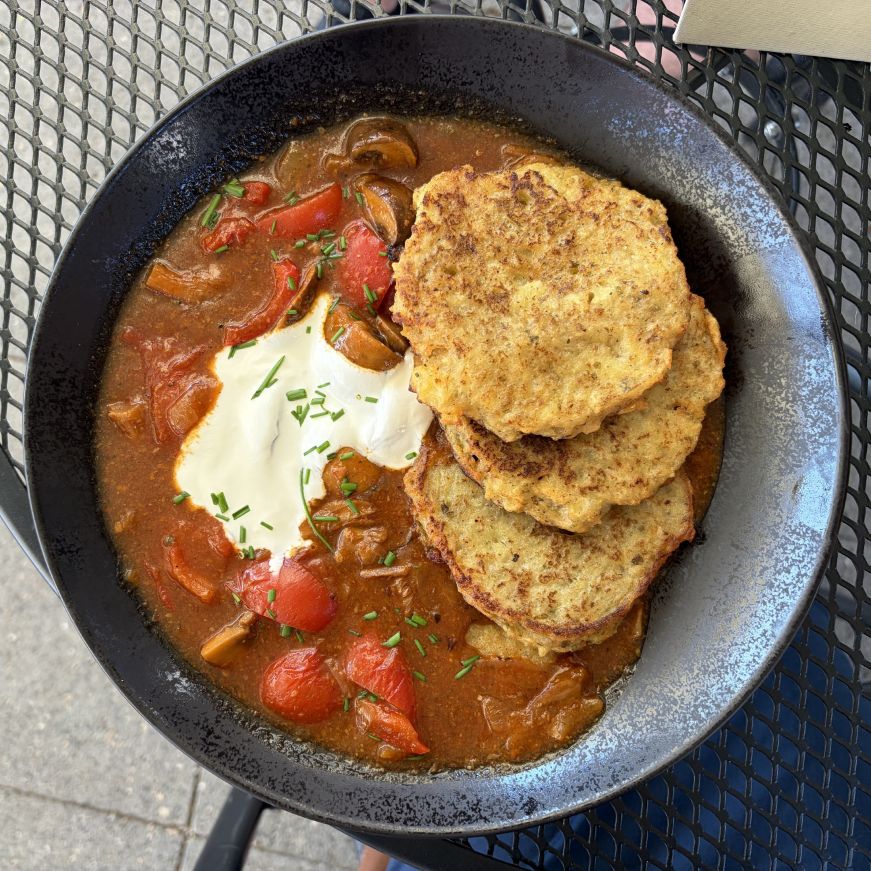 Bowl of mushroom goulash with several potato pancakes