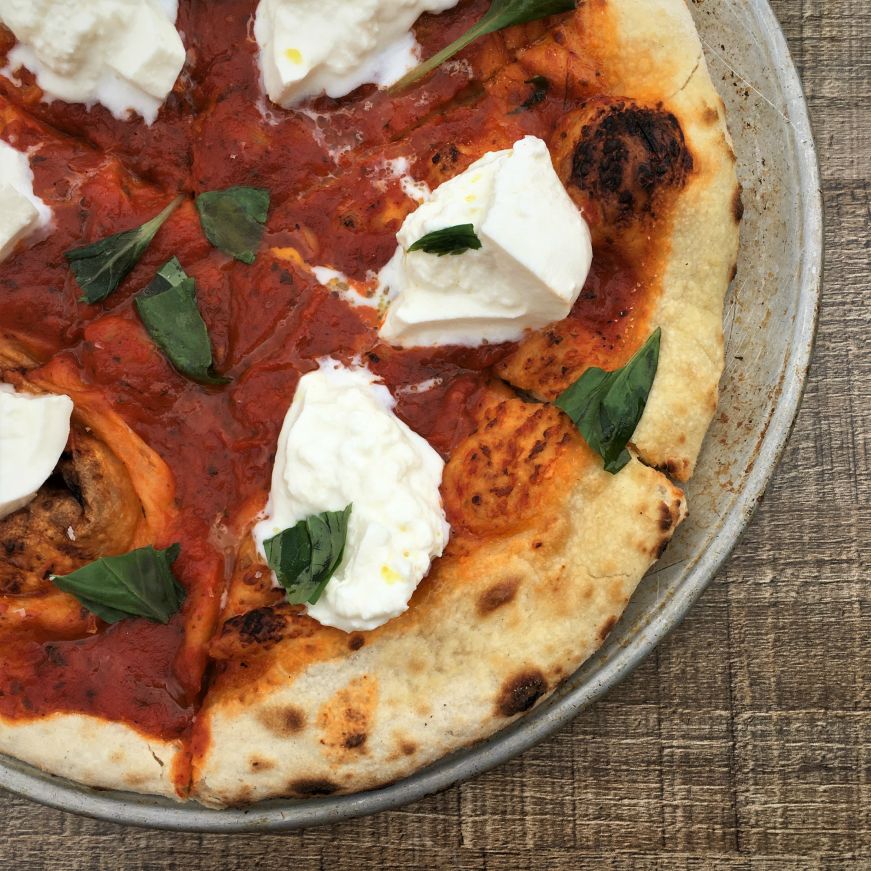 Pizza topped with tomato sauce, fresh basil leaves, and burrata