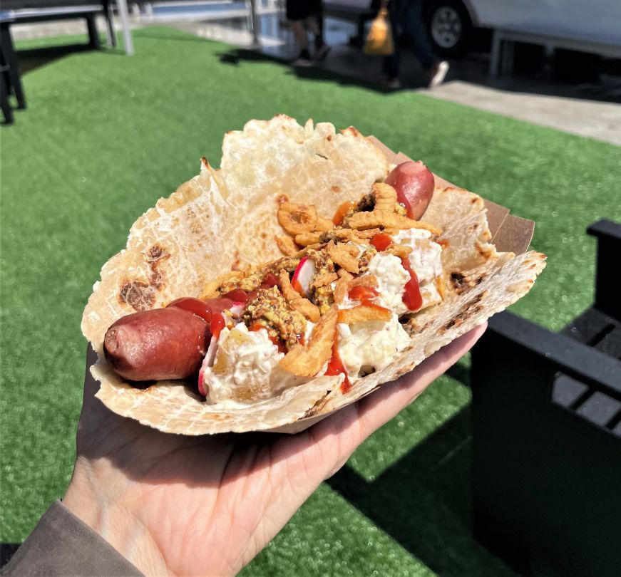 Hot dog on a piece of lefse topped with potato salad and crispy onions