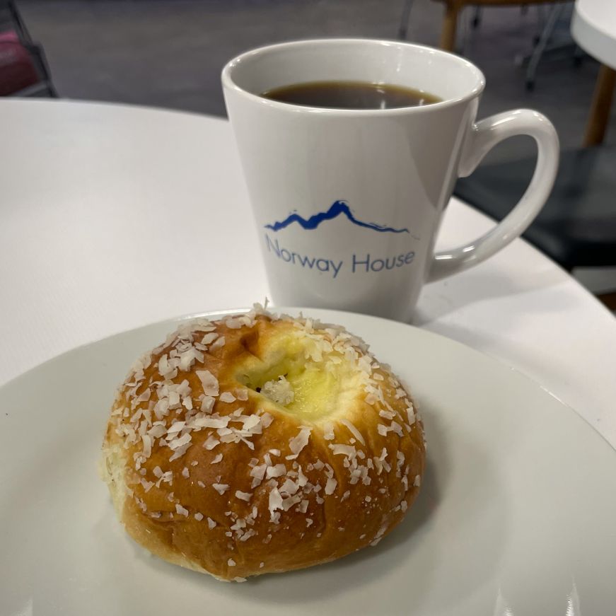 Skol bun (skolleboller), Kaffebar at Norway House Custard-filled bun topped with coconut on a plate with a Norway House coffee cup in the background