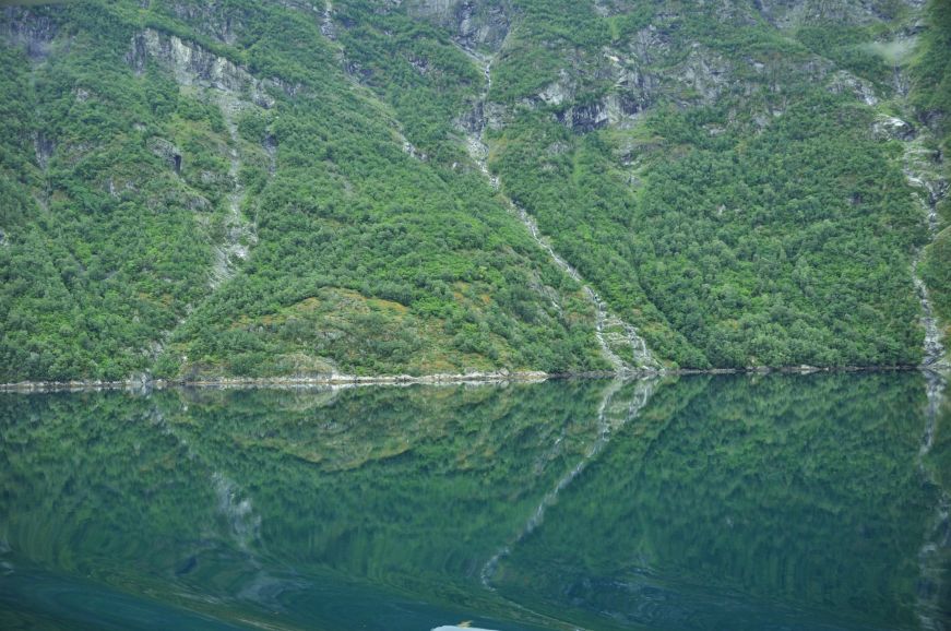 Green cliff with waterfalls trickling down into fjord below, Norway