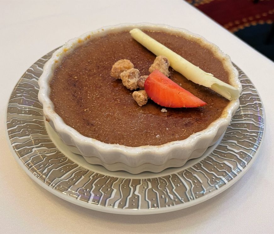 Creme brulee topped with chopped hazelnuts, a strawberry, and white chocolate curl