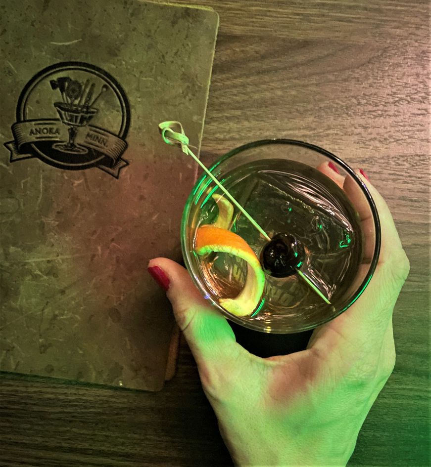 Top down view of a table with Stacy's hand holding an old fashioned and a leather menu 