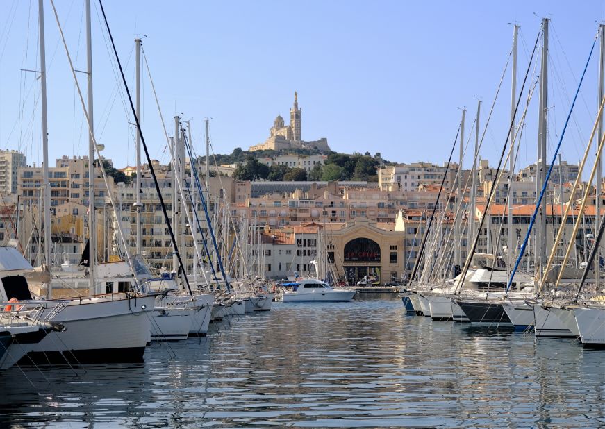 Marina filled with sailboats with a cathedral on top of a hill in the background