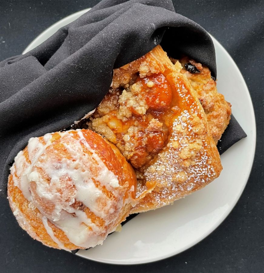 Pastries, Alma Cinnamon roll, banana caramel danish, and scone wrapped in a black napkin