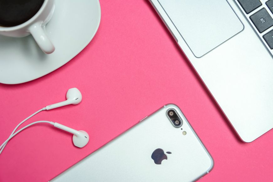 Top down view of iPhone, earphones, and laptop on a pink table