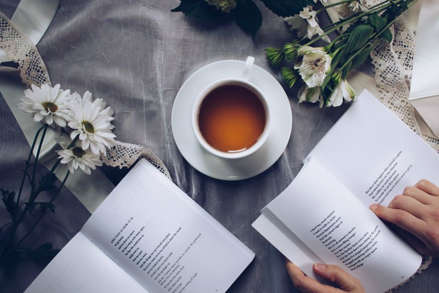 Top down view of table with open books, flowers, and a cup of tea