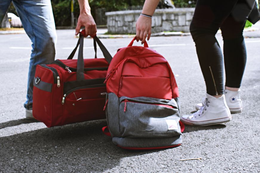 Lower bodies of people holding a duffel bag and a back pack