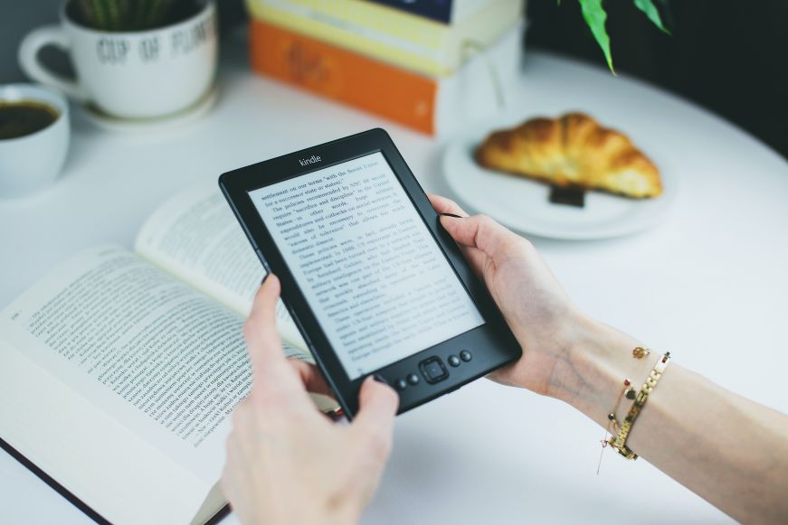 Hand holding an ereader with a croissant in the background