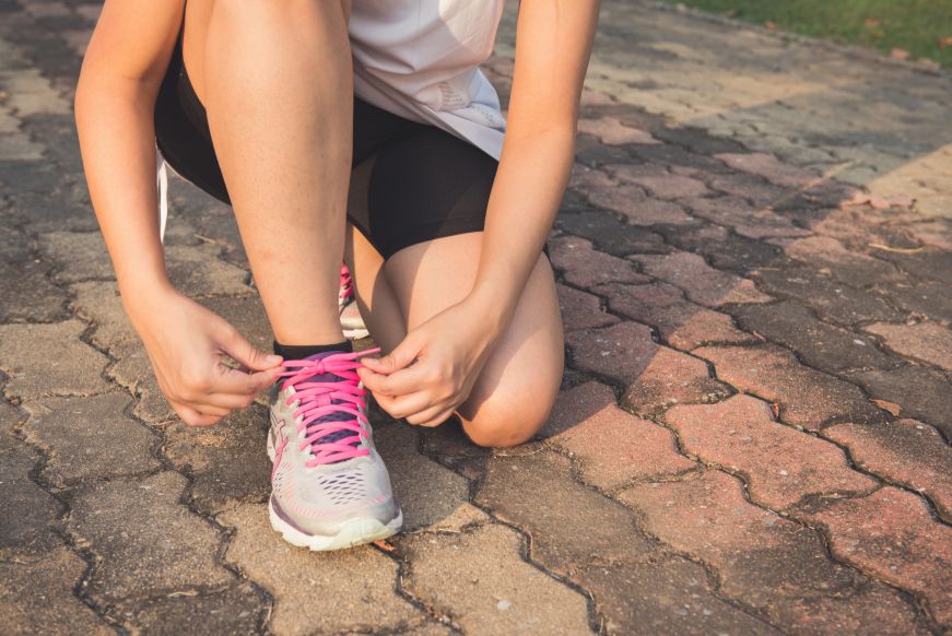 Woman kneeling on ground tying a running shoe Woman kneeling on ground tying a running shoe