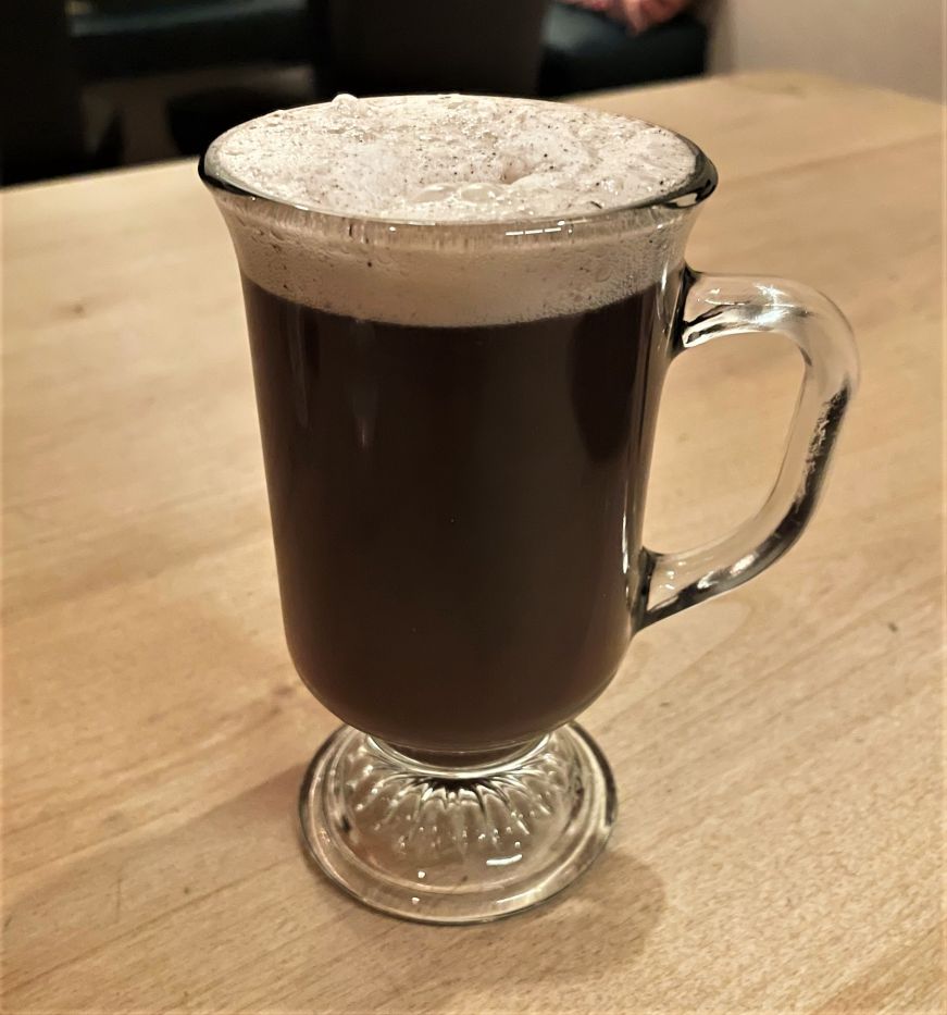 Glass mug holding a cocktail topped with foam