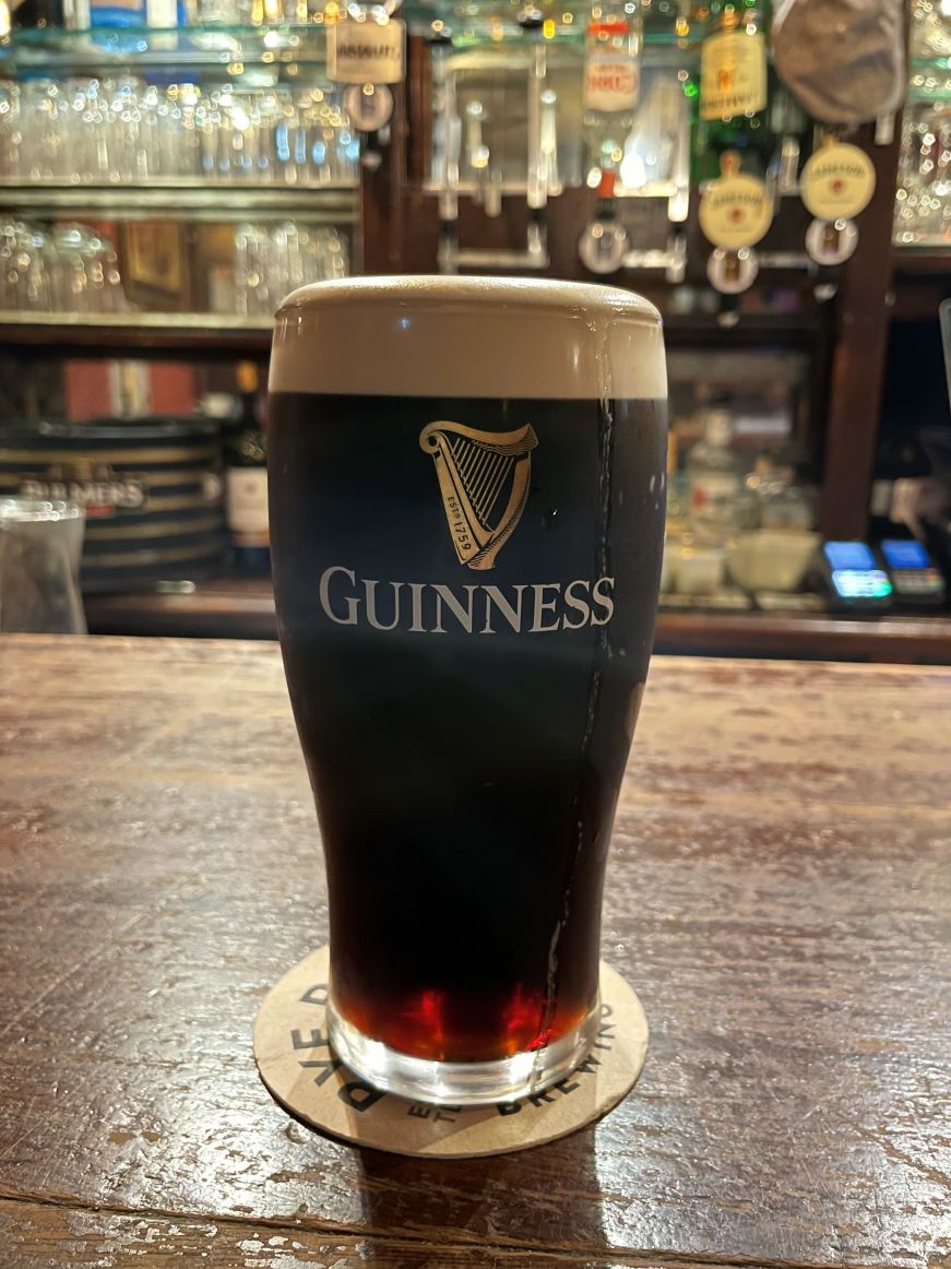 Pint of Guinness on a wooden bar with bottles and glasses in the background