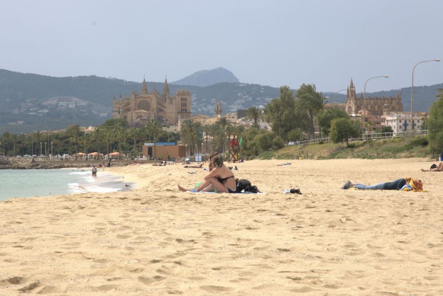 Sunbathers sitting on a beach with a cathedral in the background