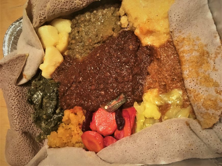 Foil pan of injera with a variety of vegetarian stews