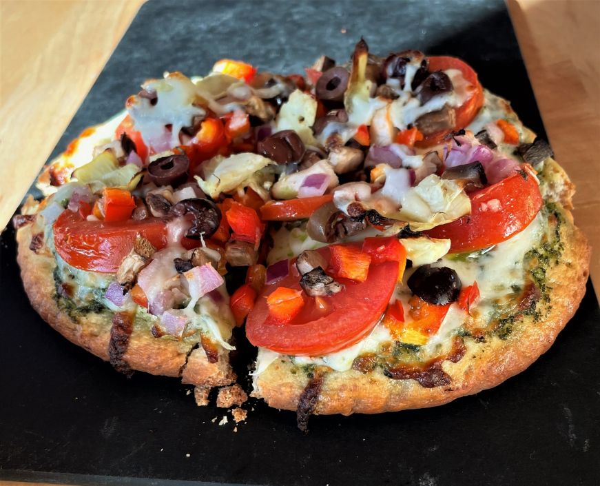 Personal-sized pizza topped with pesto and vegetables
