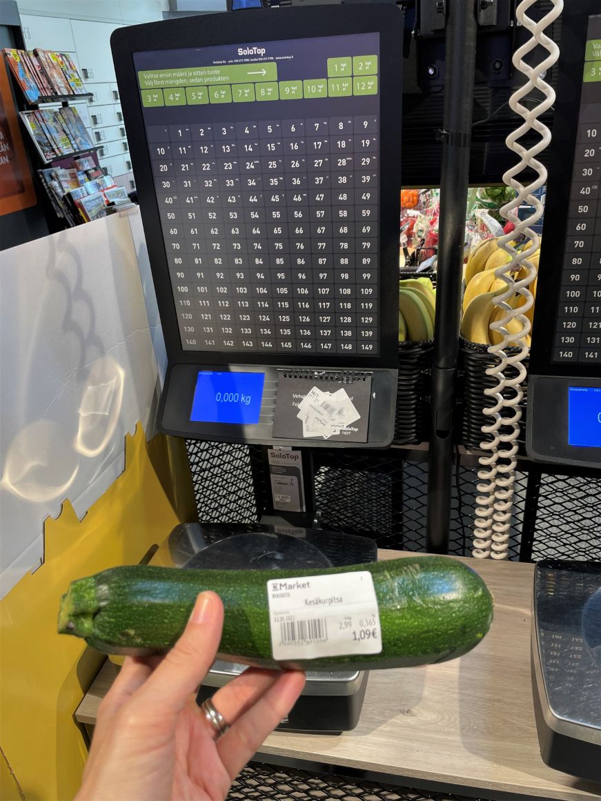 Stacy's hand holding a zucchini with a printed label with a scale and printer in the background