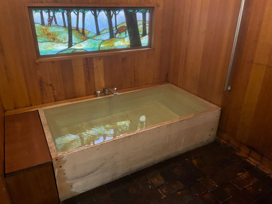 Large wooden bathtub with a stained glass window on the wall behind it