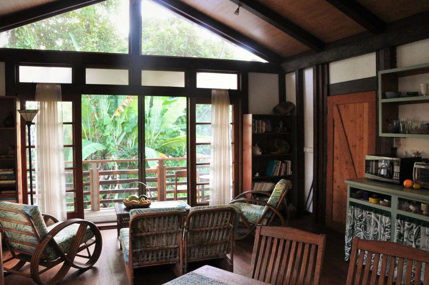 Cottage interior with a table, kitchenette, and couch with a view of lush tropical greenery through a glass door, Pua's Patch Airbnb, Papikou, Hawaii