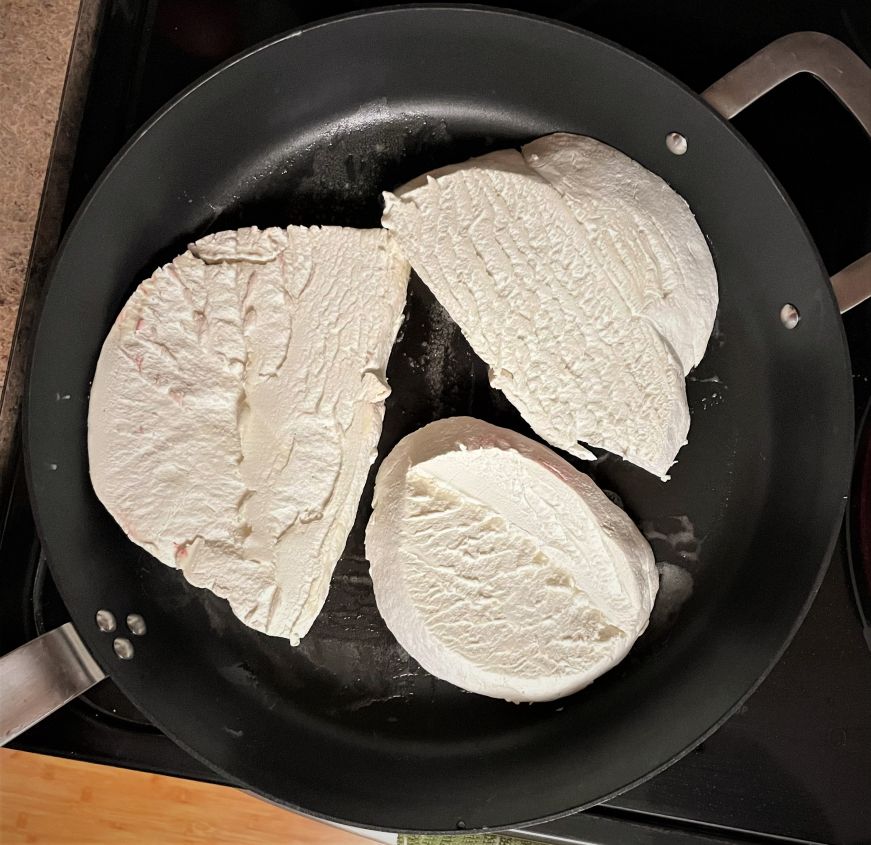 Three slices of puffball mushrooms cooking in a large skillet