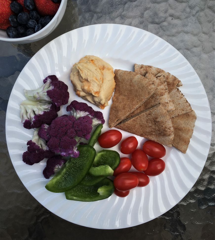 Plate of hummus, pita wedges, purple cauliflower, green pepper slices, and cherry tomatoes