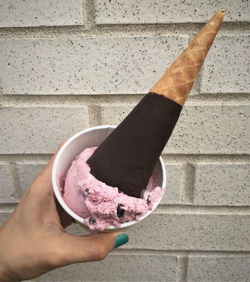 Hand holding a raspberry chocolate chip ice cream cone in a bowl