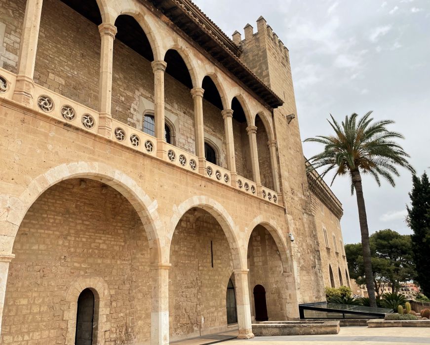 Stone building with first and second story arcades, with a palm tree beside it