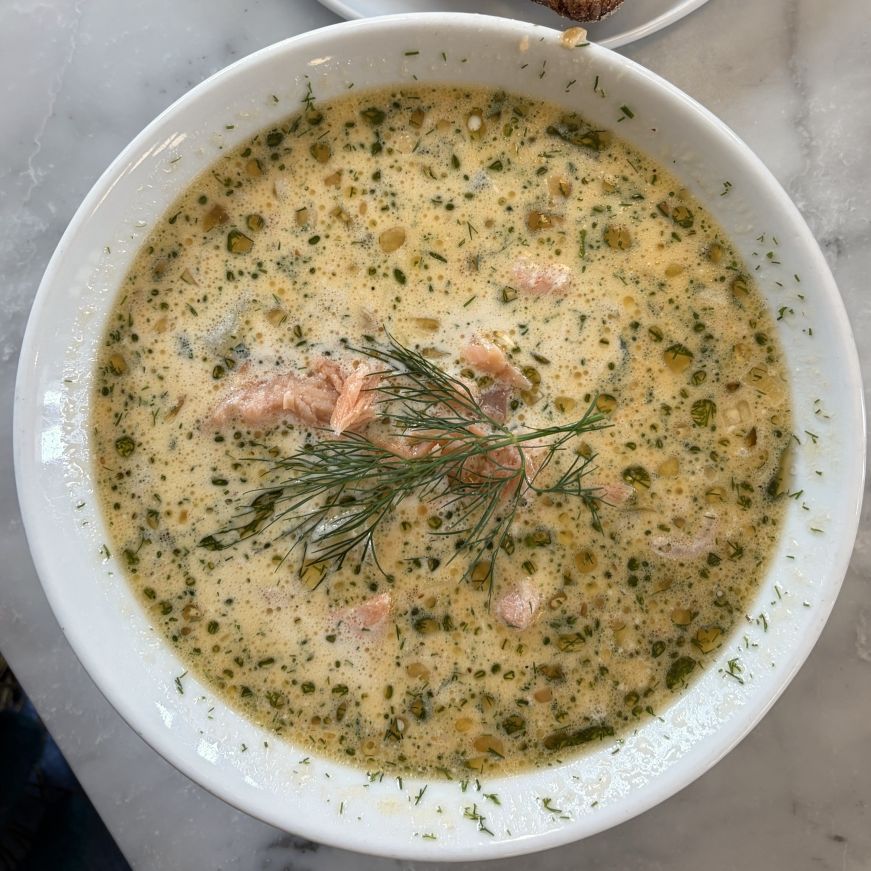 Bowl of salmon soup garnished with fresh dill and green herb oil