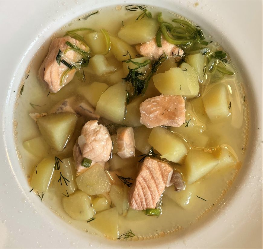 Bowl of broth-based soup with pieces of salmon and potato