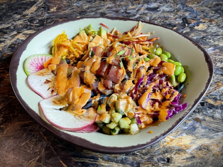 Bowl of blue noodles topped with raw tuna and colorful vegetables