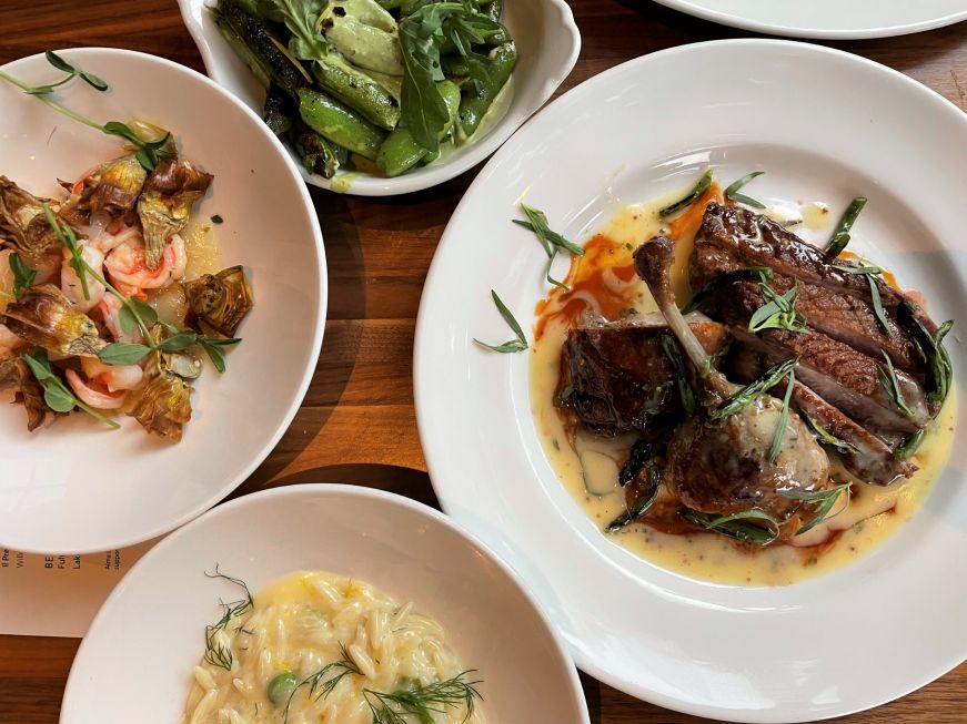 Top down view of a table with plates of prawns, roasted duck, orzo, and snap peas