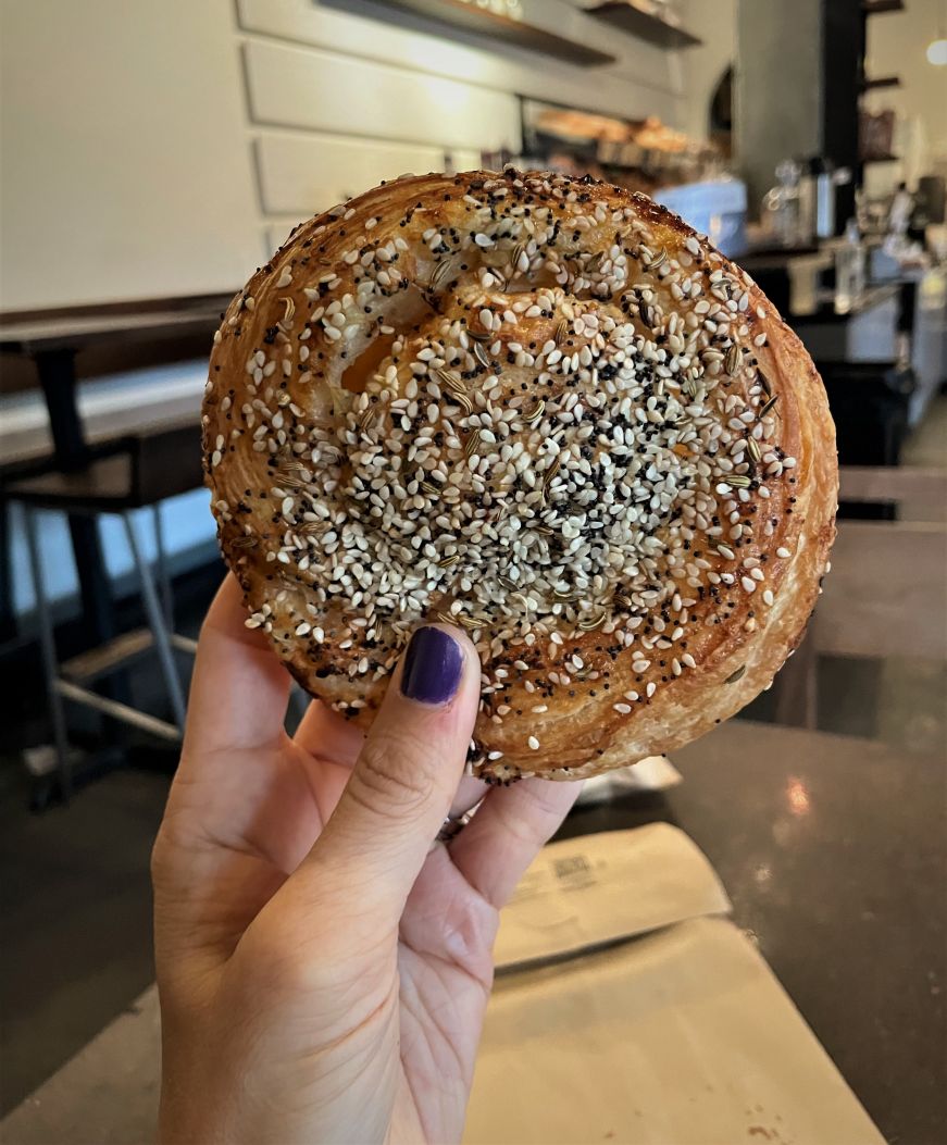 Hand holding a coiled pastry garnished with seeds