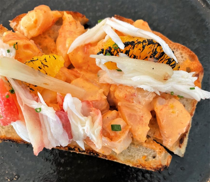 Close up view of a piece of toast topped with pieces of crab and shrimp