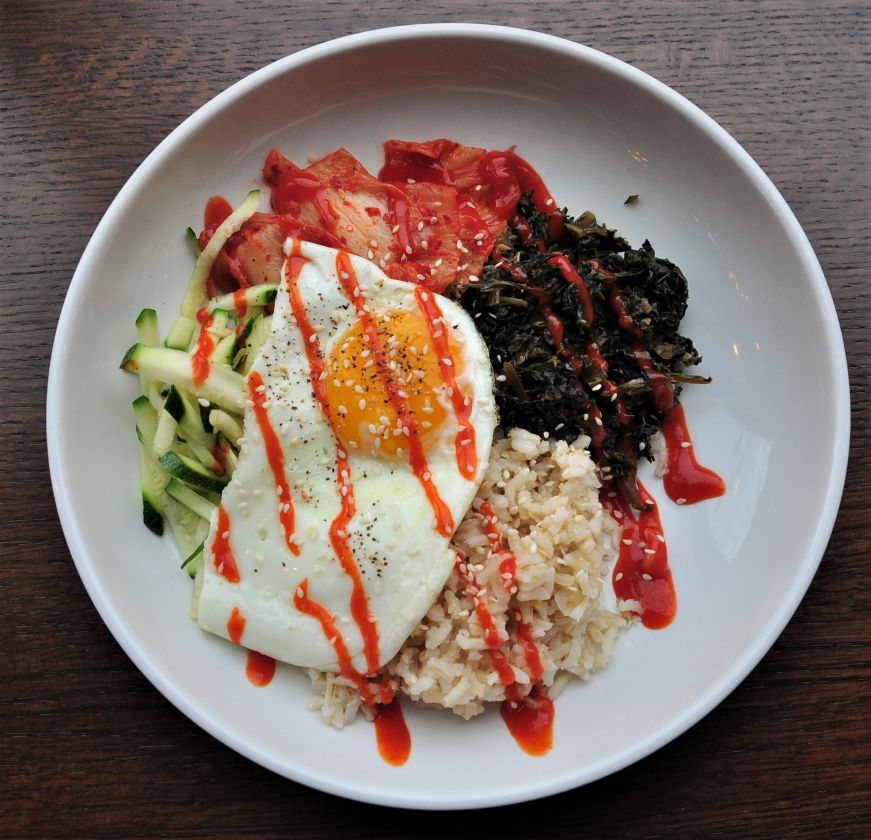 Rice bowl with kimchi Plate of rice, fried egg, kimchi, and kale drizzled with hot sauce