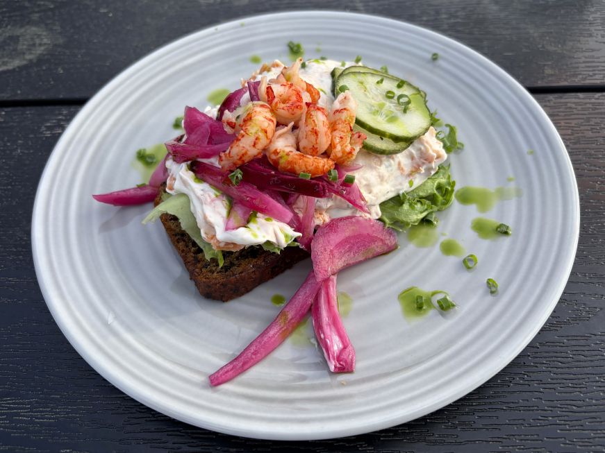 Slice of rye bread topped with salmon salad, shrimp, red onions, and cucumbers