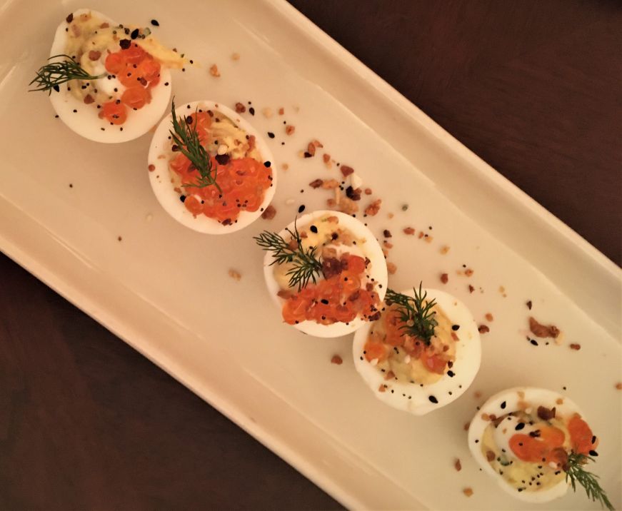 Top down view of a plate of deviled eggs garnished with caviar and dill