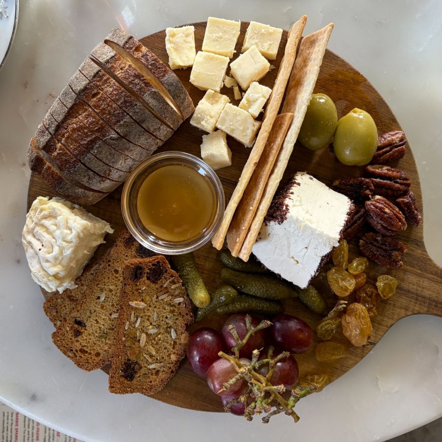 Cheese board with bread, crackers, grapes, honey, and other accompaniments