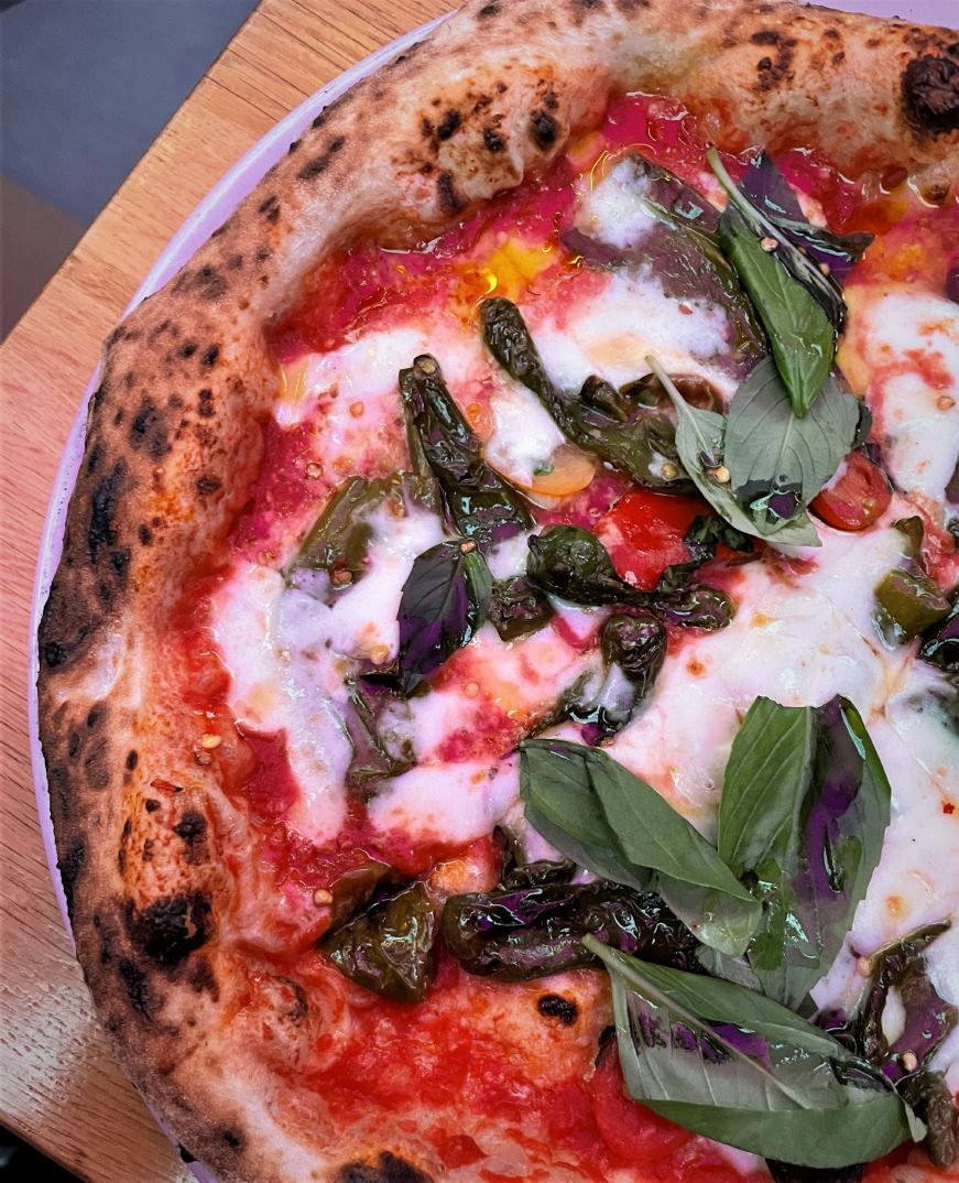 Neapolitan-style pizza topped with fresh basil leaves and peppers